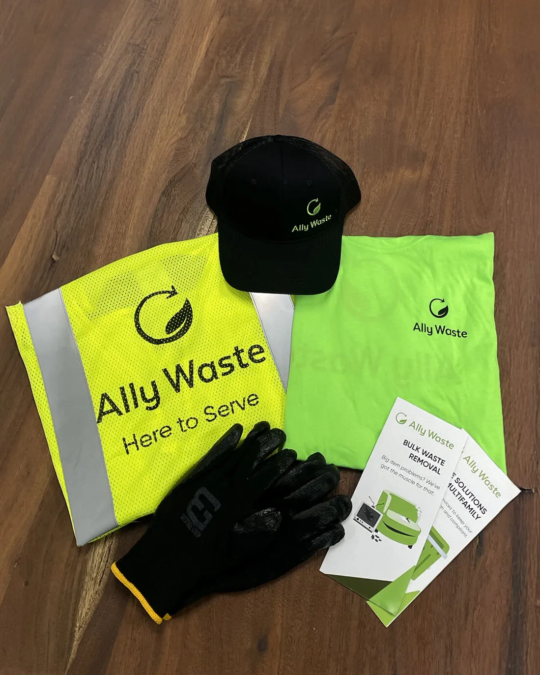Ally Waste gear laid out: a hat, a high-visibility vest reading Here to Serve, a shirt, gloves and service flyers